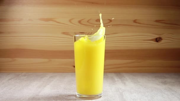 Glass with orange juice on the table. Ice cubes fall into the juice, creating a lot of splashing. Slow motion - Video, Çekim