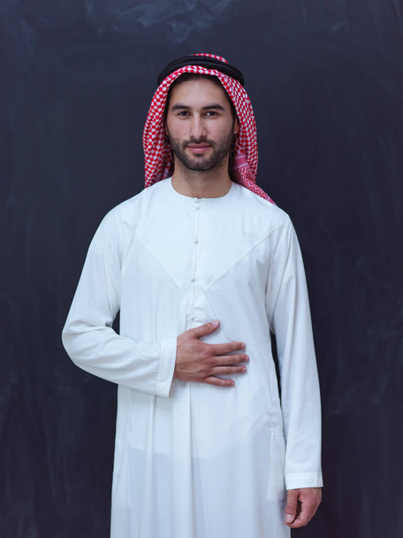 portrait of young arabian man in traditional clothes in front of black chalkboard representing modern islam fashion and ramadan kareem concept - Φωτογραφία, εικόνα