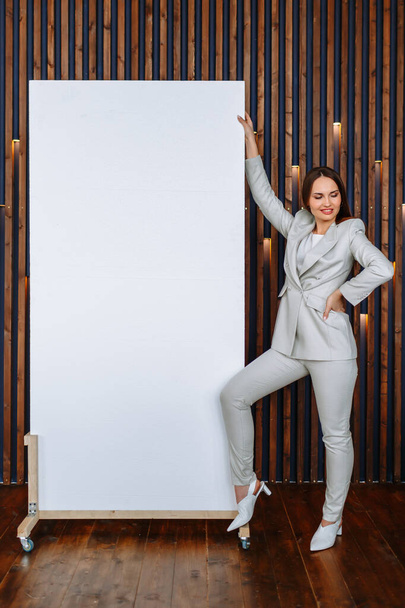 Uma garota modelo em um terno de negócios mostra uma tela branca na qual você pode escrever um slogan ou informações de publicidade
 - Foto, Imagem