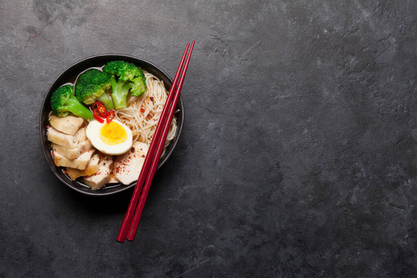 Asijská nudlová ramenová polévka s kuřetem, zeleninou a vejci na kamenném pozadí. Horní pohled plochý ležel s kopírovacím prostorem - Fotografie, Obrázek