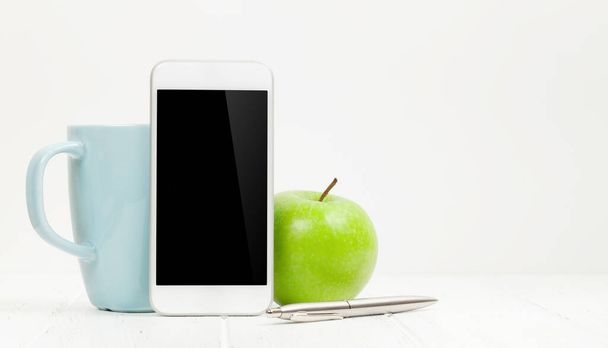 Escritório mesa de trabalho com smartphone, maçã e xícara de café sobre fundo branco. Com espaço para o seu texto ou aplicativo
 - Foto, Imagem