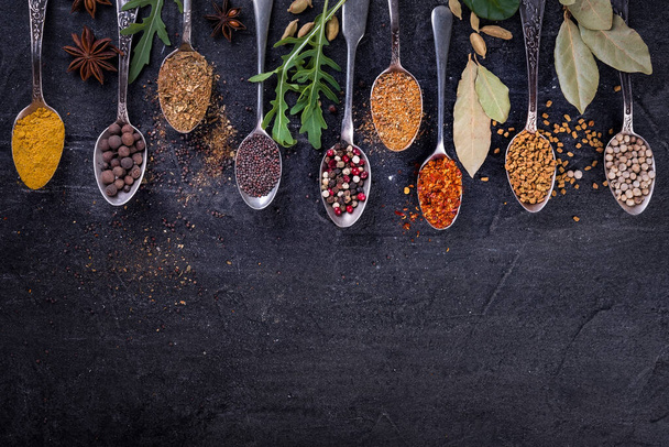 Spices and herbs on spoons in  a black background, top view.  Indian cuisine.   - Photo, Image