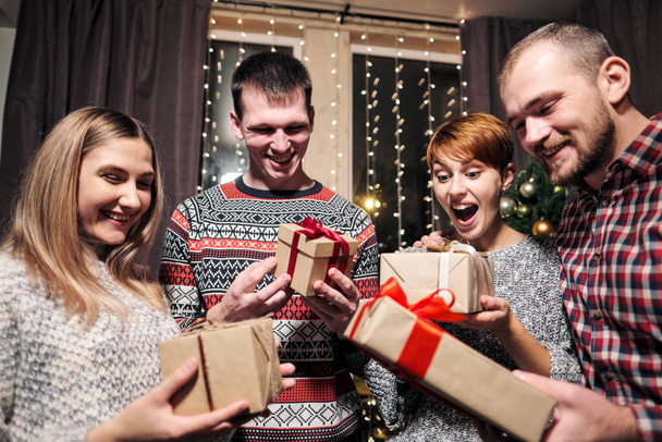 Группа друзей, мужчин и женщин, празднуют Рождество. Они дарят друг другу подарки, радуются и смеются. Новогодняя ночь
. - Фото, изображение