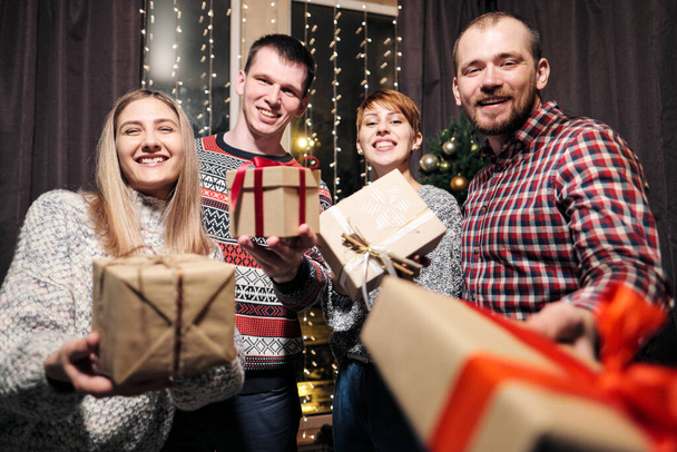 Un grupo de amigos, hombres y mujeres, celebran la Navidad. Se dan regalos, se regocijan y se ríen. Nochevieja
. - Foto, Imagen