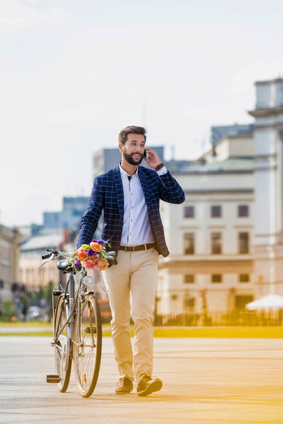 Portrait of young attractive businessman holding bouquet of flowers while talking on smartphone - Foto, immagini