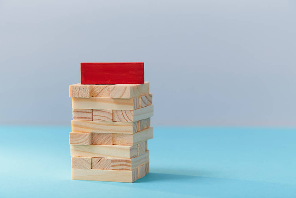 Wooden tower of cubes with red plank on top, copy space. Business planning and strategy. Teamwork, teambuilding concept - Fotoğraf, Görsel