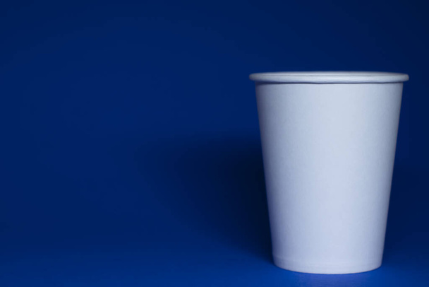 Ένα άδειο λευκό χάρτινο κύπελλο σε μπλε φόντο. οριζόντια φωτογραφία.  - Φωτογραφία, εικόνα
