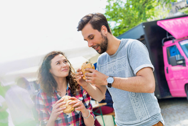 Young attractive couple eating hamburgers against food truck - Foto, afbeelding