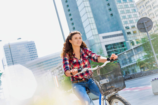 Portrait of young beautiful woman smiling while riding bicycle in the middle of the city - Fotografie, Obrázek