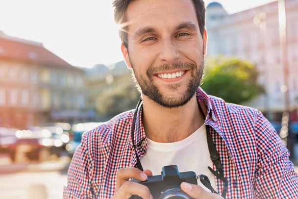 Young attractive man holding camera and taking photo - Photo, image
