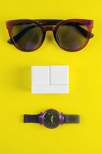 Das Reisekonzept. Gläser, Armbanduhr und weiße Holzwürfel, auf denen die Eingabe des Datums steht, stehen auf gelbem Hintergrund. Top-Ansichten. - Foto, Bild