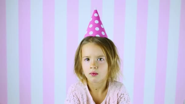 Kis szőke lány egy meglepetés erejéig, mosolyogva a szülinapi rózsaszín sapkában Gyermek otthon ünnepli a születésnapját. Boldog szülinapot.. - Felvétel, videó