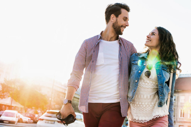 Portrait of young attractive couple walking in the middle of the city with lens flare in background - Fotoğraf, Görsel