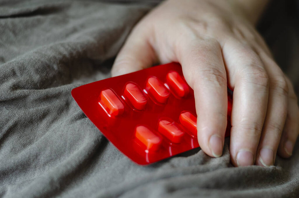 Weibliche Hand liegt auf der Decke und hält eine Blase mit Tabletten. Blister medizinischer Pillen gegen sexuelle Dysfunktion. Prävention und Behandlung sexueller Dysfunktion bei Frauen. Selektiver Fokus. - Foto, Bild