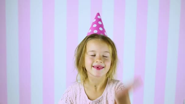 Kis szőke lány a meglepetésig, mosolygós szülinapi rózsaszín sapkában - Felvétel, videó