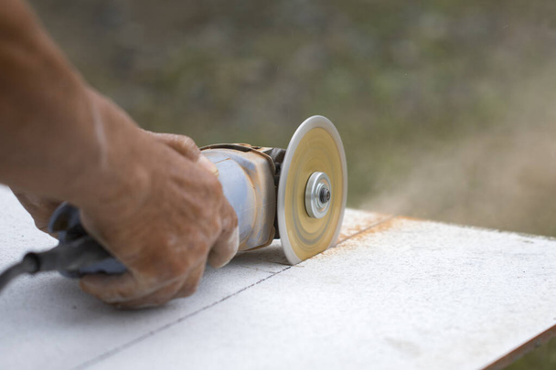 Imagem do trabalhador usando a ferramenta para cortar telha com poeira no fundo
. - Foto, Imagem