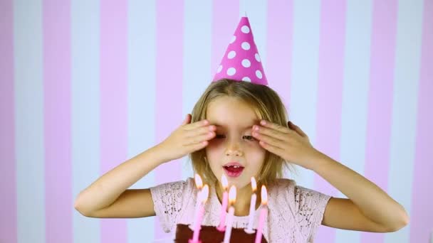 Gelukkige verrassing, ogen dicht meisje met roze pet die kaarsen blaast op een verjaardagstaart - Video