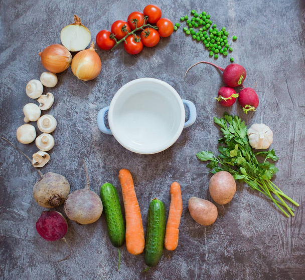 Состав со свежими овощами на сером фоне, место для текста. Маленький пустой горшок на круге свежих овощей
 - Фото, изображение