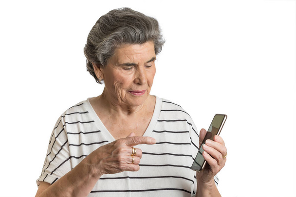 Oudere vrouw in groep risico tijdens pandemie van coronavirus met behulp van mobiele telefoon geïsoleerd op witte achtergrond - Foto, afbeelding