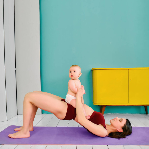 woman practicing yoga at home with a small child - Valokuva, kuva