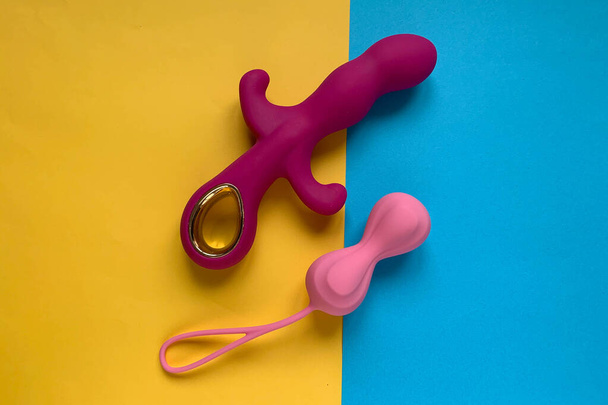 Seks speelgoed. Roze vibrator en wiebelballen op een geel-blauwe achtergrond. Handig voor volwassenen - Foto, afbeelding
