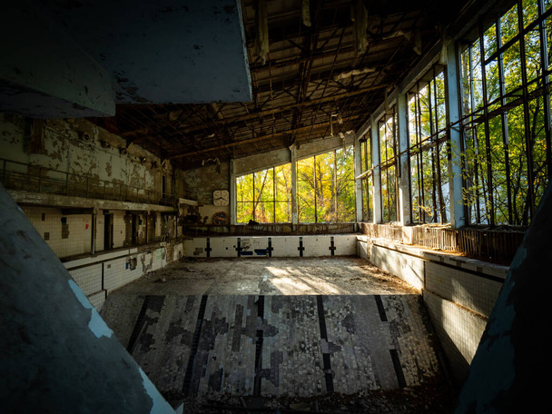 Заброшенный пустой бассейн в школе в Припяти, недалеко от Чернобыля, Украина. Окружение спортзала заросло деревьями и кустарниками
. - Фото, изображение