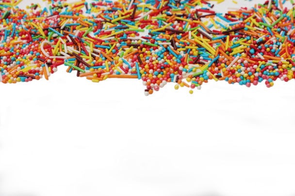 snoepgoed poeder voor het versieren van cupcakes en cakes. Decoratieve hagelslag rand op witte achtergrond. Multicolor Suikerwerk poeder in de hoek. Verspreid zoet suikerstokje en ballen. - Foto, afbeelding