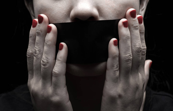 Concept on the topic of freedom of speech, censorship, freedom of press. International Human Right day: the girl's face is sealed her mouth with black paper - 写真・画像