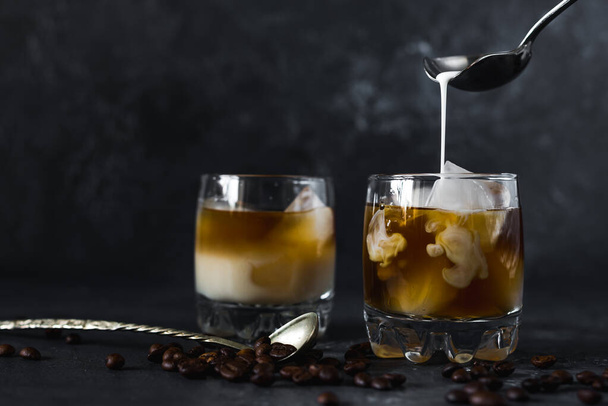 Pouring milk into a glass of cold tasty aromatic coffee with ice on a dark background - Photo, Image