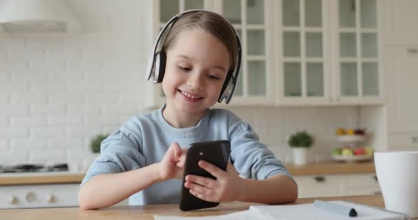 Cute school girl wearing headphones using smart phone at home - Séquence, vidéo