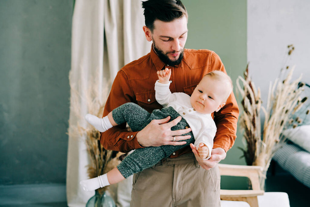 nuori tyylikäs isä trendikkäässä oranssissa paidassa leikkii nuoren poikansa kanssa ruskeassa hatussa sylissään tilavassa tyylikkäässä studiossa
. - Valokuva, kuva