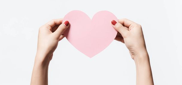 Close up women holding pink blank  paper with heart shape on white background. Free space, ready for type with text banner. Valentine's day concept - 写真・画像