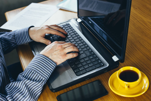 Hombre escribiendo con la taza del ordenador portátil y del café en la tabla de madera. Filtro vintage tonificado
. - Foto, Imagen