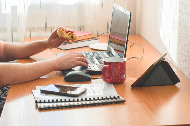 Um homem a trabalhar de casa. Usando computador e comendo donuts. Trabalho à distância ou educação on-line ou ficar em casa conceito
.  - Foto, Imagem
