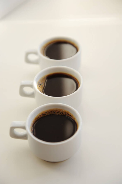 Three white cups with black coffee one after another on white background - Фото, зображення