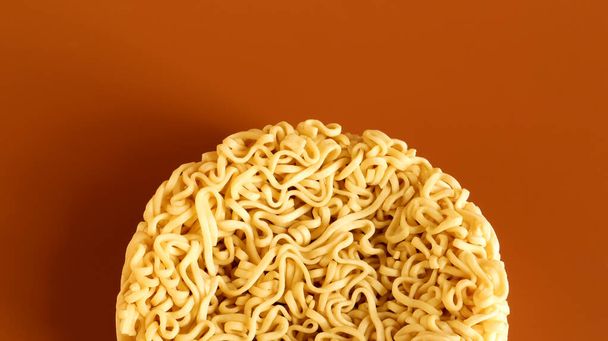 Korean instant noodles in the shape of a circle on a brown background. A yellowish-white dried raw vermicelli with long round lines and twisted in different directions into a briquette - Photo, Image