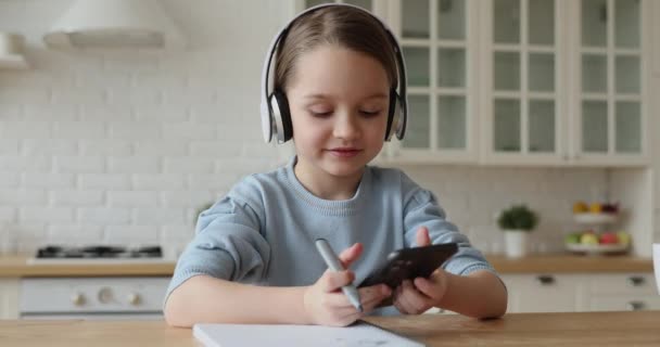 Child girl wearing headphones studying by mobile videocall with tutor - Séquence, vidéo