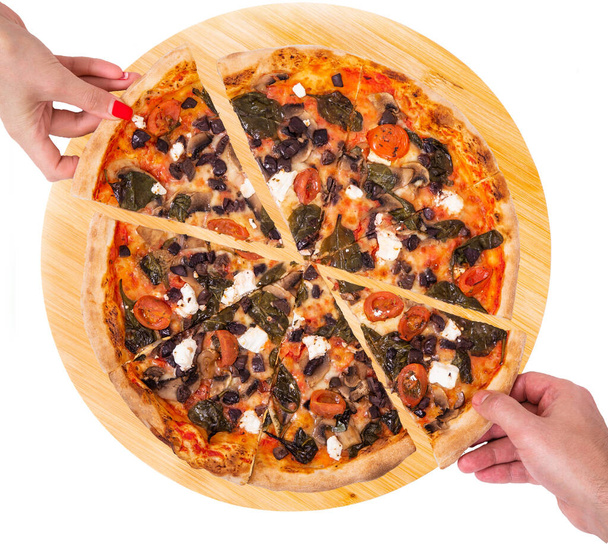 Primo piano di persone mani che prendono fette di pizza con pomodorini, spinaci, mozzarella, feta, kalamata oliva e funghi dal piatto di legno isolato su sfondo bianco, vista dall'alto
 - Foto, immagini