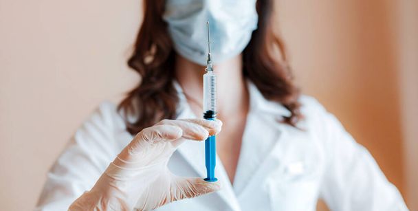 Медицинский шприц в руке врача крупным планом. Медицинское пластиковое оборудование для вакцинации с помощью капли иглы. вакцина COVID-19 coronavirus
 - Фото, изображение