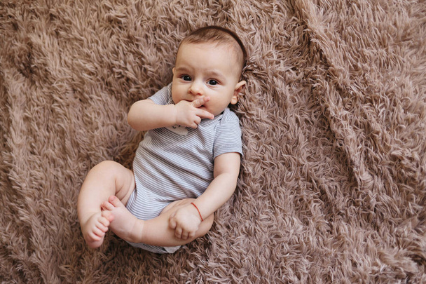 portrait of a child 4 months old lying on the bed and looking. Charming child with dark eyes lying on back, - Photo, Image