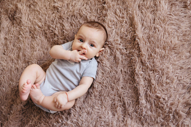 portrait of a child 4 months old lying on the bed and looking. Charming child with dark eyes lying on back, - Foto, Imagen