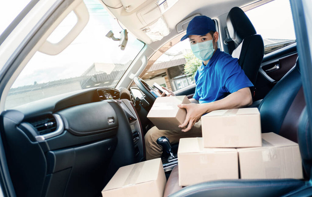 Asian Delivery man wearing mask send a package holding smartphone on front home receiver shipping deliver cargo social distancing, Many parcel in hatchback car while the virus is spreading medical. - Photo, Image