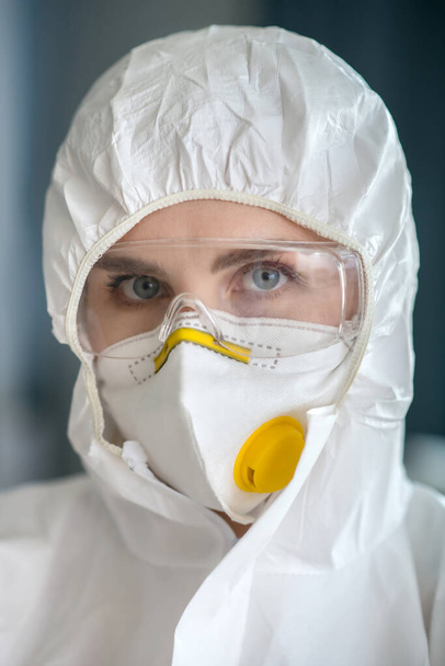 Woman in white workwear and protective eyeglasses looking serious - Фото, изображение