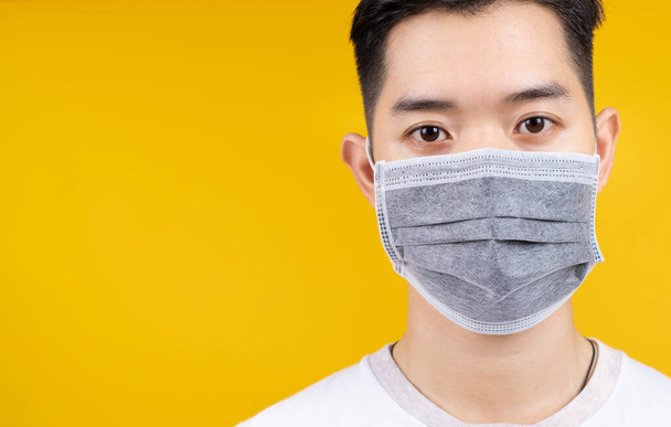 Close up Face of man wearing medical mask protection against germs from crisis coronavirus, covid-19 and prevent infection on yellow background isolated studio shot with copy space the left. - 写真・画像