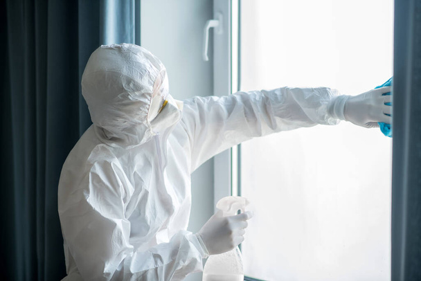 Woman in white workwear and respirator cleaning the window - Valokuva, kuva