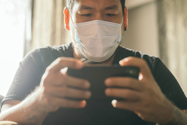Concept of coronavirus quarantine. Man with medical face mask using the phone to search for news in the house. - Foto, Imagem