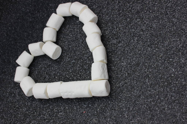 Marshmallows in Herzform isoliert auf grauem Steingrund aufgebahrt. Ein Bündel kleiner weißer Marshmallows in Herzform liegt auf einem Tisch. Süßigkeiten aus nächster Nähe. - Foto, Bild