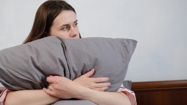Unhappy young woman sitting on bed, feeling depressed, thinking about problems, bad relationship or break up, upset girl embraces grey pillow, feeling lonely, suffering from psychological troubles - Video