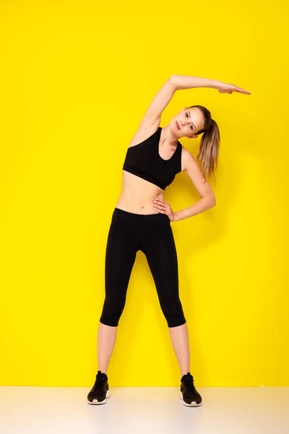 Sporty woman on yellow background. Photo of attractive woman in fashionable sportswear. Doing some streching movement before the execise - Valokuva, kuva