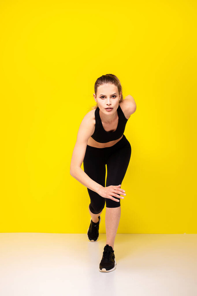 Sporty woman runner in silhouette on yellow background. Photo of attractive woman in fashionable sportswear. Dynamic movement. Side view. Sport and healthy lifestyle - Photo, Image